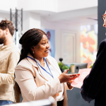 Friendly smiling African American woman shop sales assistant explaining senior man customer Black Friday shopping rules in clothing store. Retail worker holding sales flyer talking with shopper